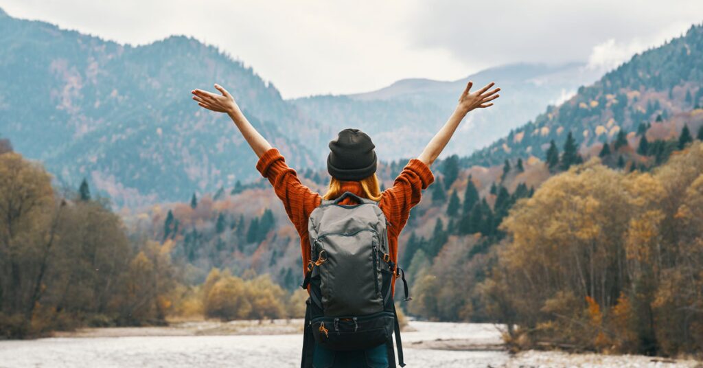 A woman happily backpacking and enjoying a beautiful mountain vista