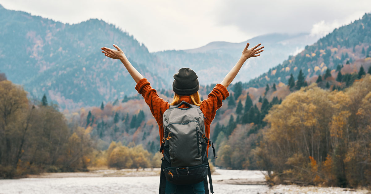 A woman happily backpacking and enjoying a beautiful mountain vista